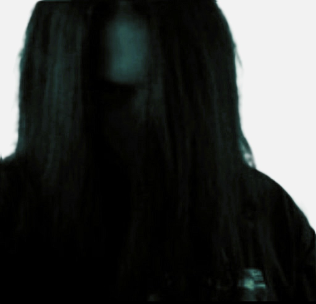 A figure with long dark hair partially obscured, set against a light background, creating a mysterious atmosphere.